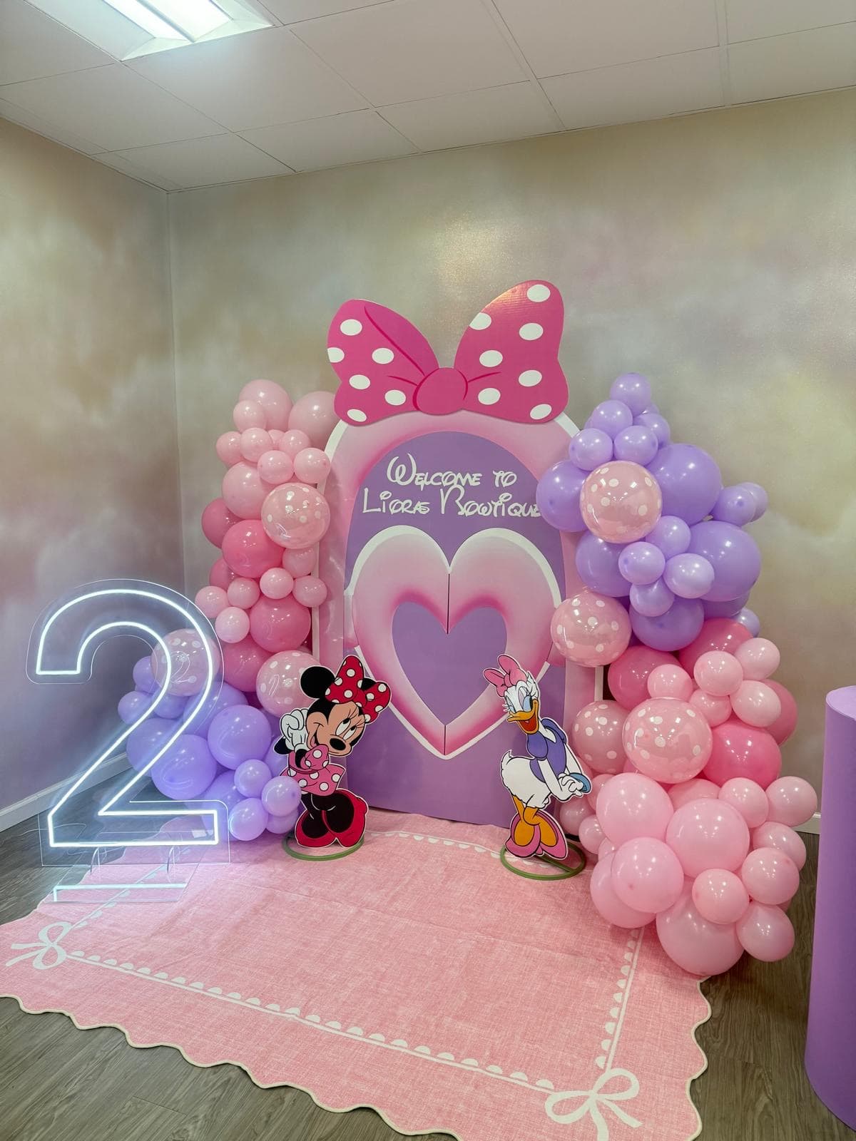 Minnie Mouse themed party backdrop with neon number 2 and pink and purple balloon garland